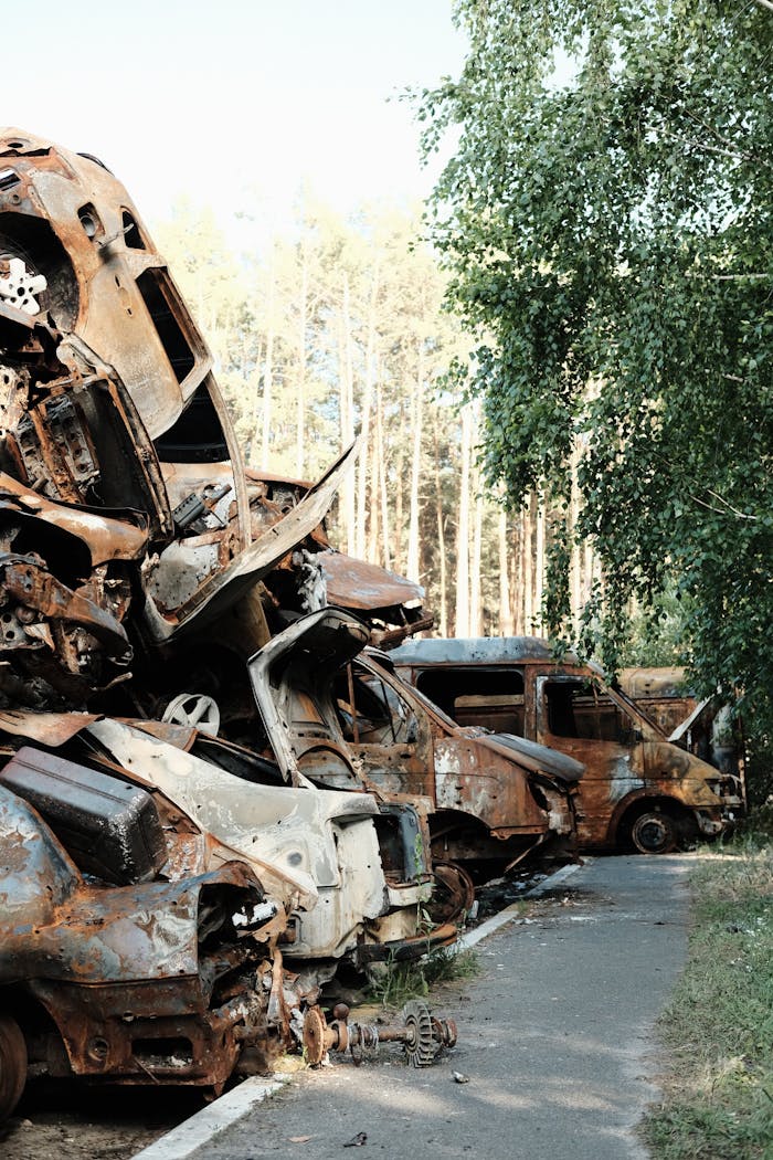 A pile of corroded and wrecked cars stacked in an outdoor junkyard setting.