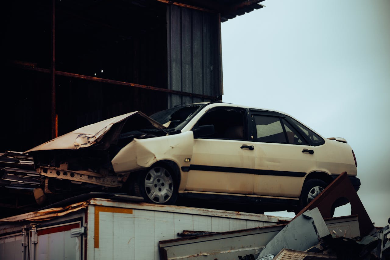 A damaged car sits atop a metal scrap heap, showing a scene of automotive decay.